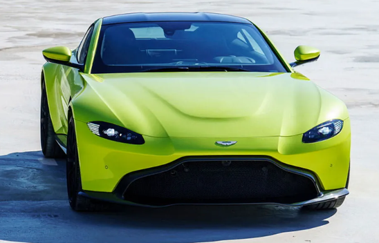 Lime green Aston Martin Vantage car sitting idle on the beach. All you can see of the beach is grey sand. It is a very peaceful atmosphere. The car is facing the camera. 1141