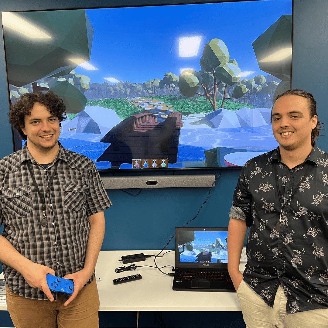 Photo of two young men standing in front of a large screen smiling at the camera