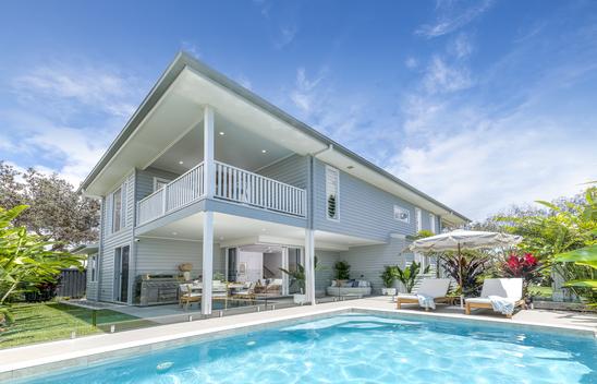 External image of the back of the house. A pool is in the foreground. Two daybeds and a sun shade umbrella on the right hand side. Lower level covered alfresco area with dining setting, BBQ and a daybed.