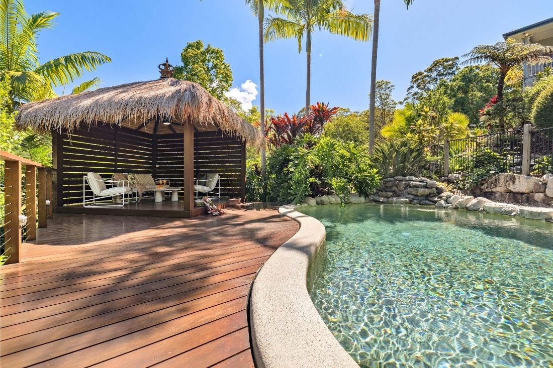 Bali hut with seating beside a pool with gardens and decking