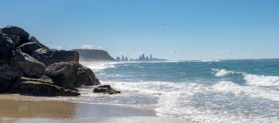 Ocean waves coming up to the rocks at Palm Beach, with the Gold Coast skyline in the background