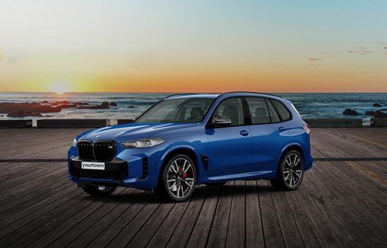 A blue BMW X5 M60i parked on a beachside pier at sunset.