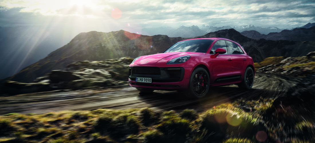 Red Porsche Macan Driving in open area with mountains behind 