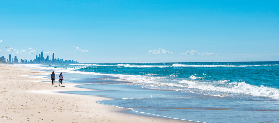 Two people walking on Mermaid Beach with the Gold Coast cityscape in the background