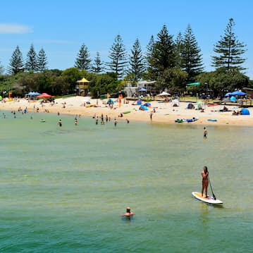 Beach scene with paddleboarder and swimmer in the foreground and crowds on the sand in the background