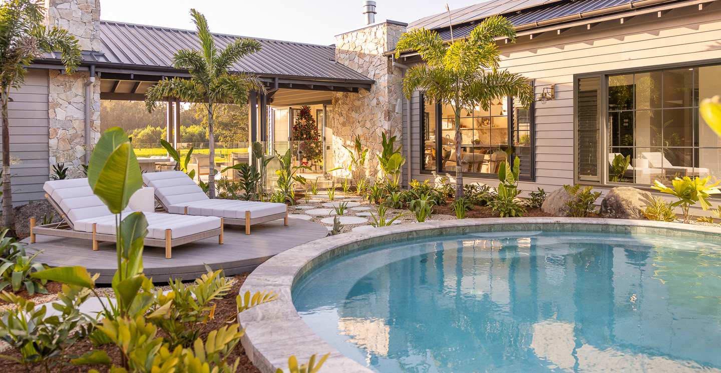 Circular pool surrounded by lush garden with 2 white recliners.