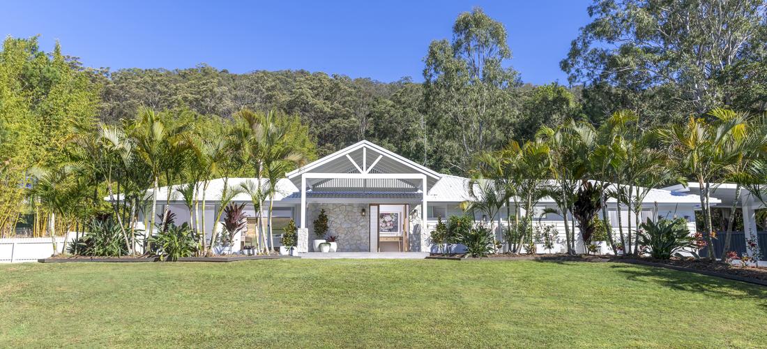 A front of house shot angled from directly in front of the house showing a big lawn and garden surrounding the home.