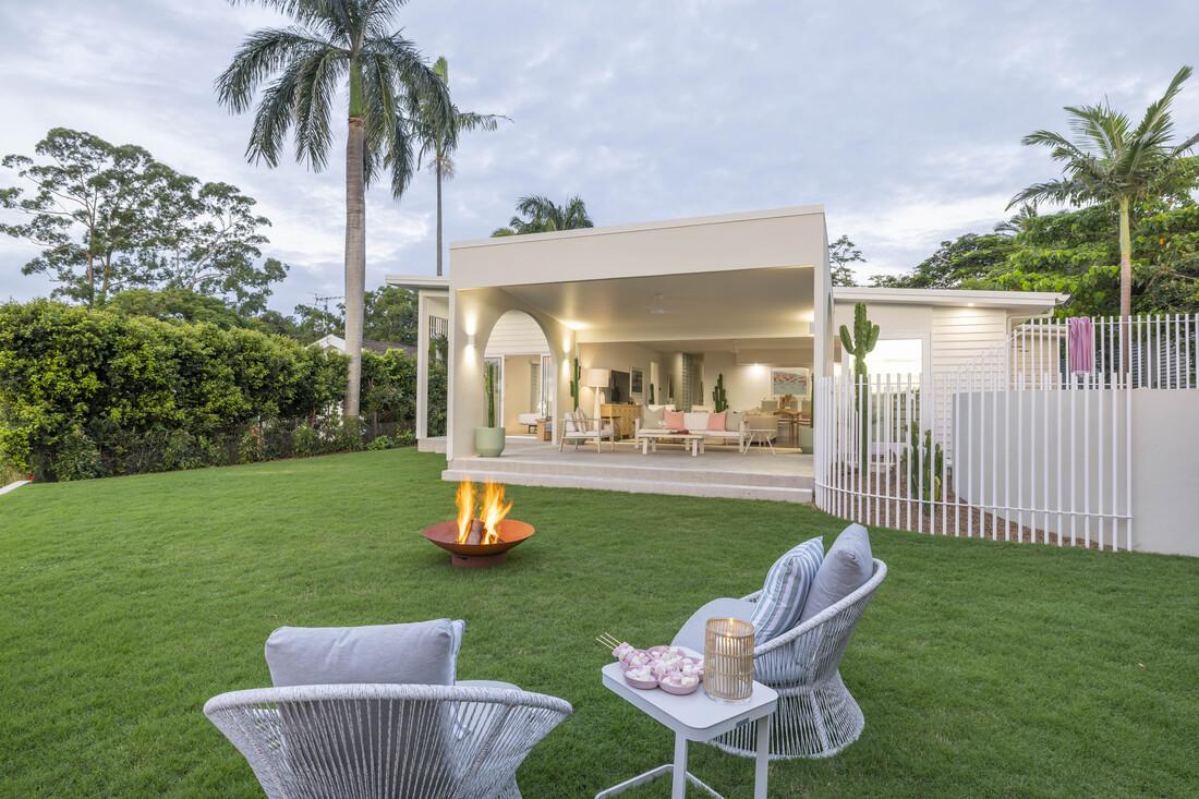 Lawn and firepit with 2 chairs and table looking into the Alfresco area.