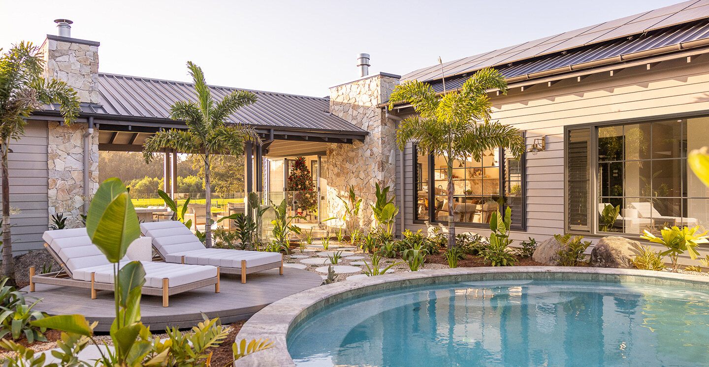 Circular pool surrounded by lush garden with 2 white recliners.