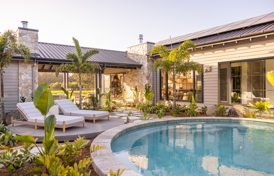 Circular pool surrounded by lush garden with 2 white recliners.