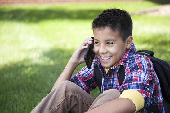 Cheerful Young Boy Using A Smart Phone In A Park